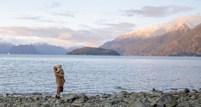A mum carrying her toddler looking out over a lake to the snow capped mountains