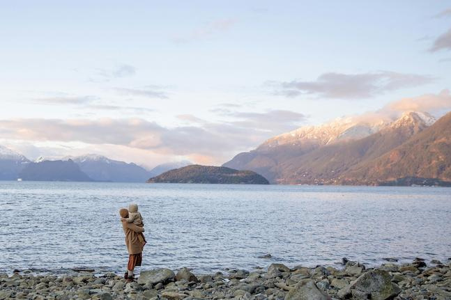 A mum carrying her toddler looking out over a lake to the snow capped mountains