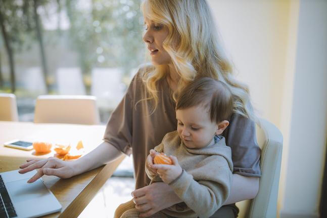 A mother with her child on her lap trying to also work on a laptop